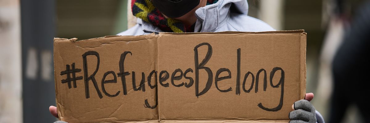 A protester carries a sign saying "#Refugees belong."