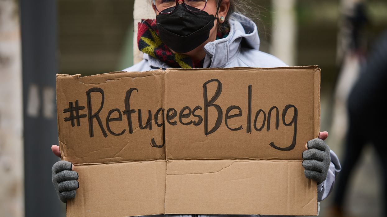 A protester carries a sign saying "#Refugees belong."