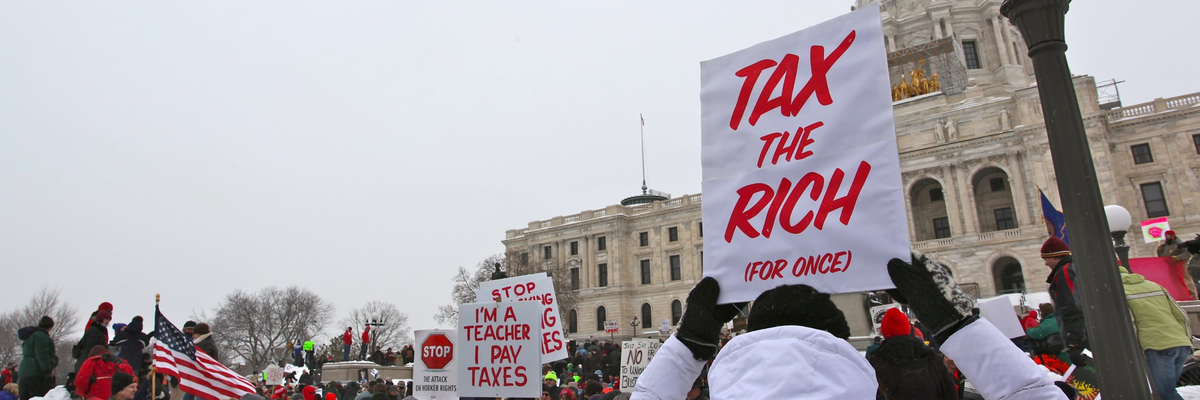 A protester carries a white sign reading, "Tax the rich," in red ink.