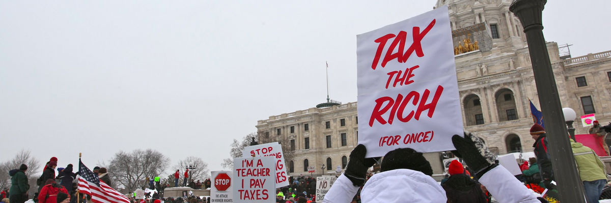 A protester carries a white sign reading, "Tax the rich," in red ink. 