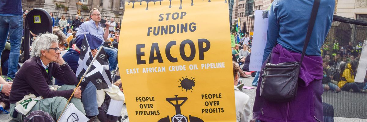 A protester carries a yellow sign protesting EACOP.