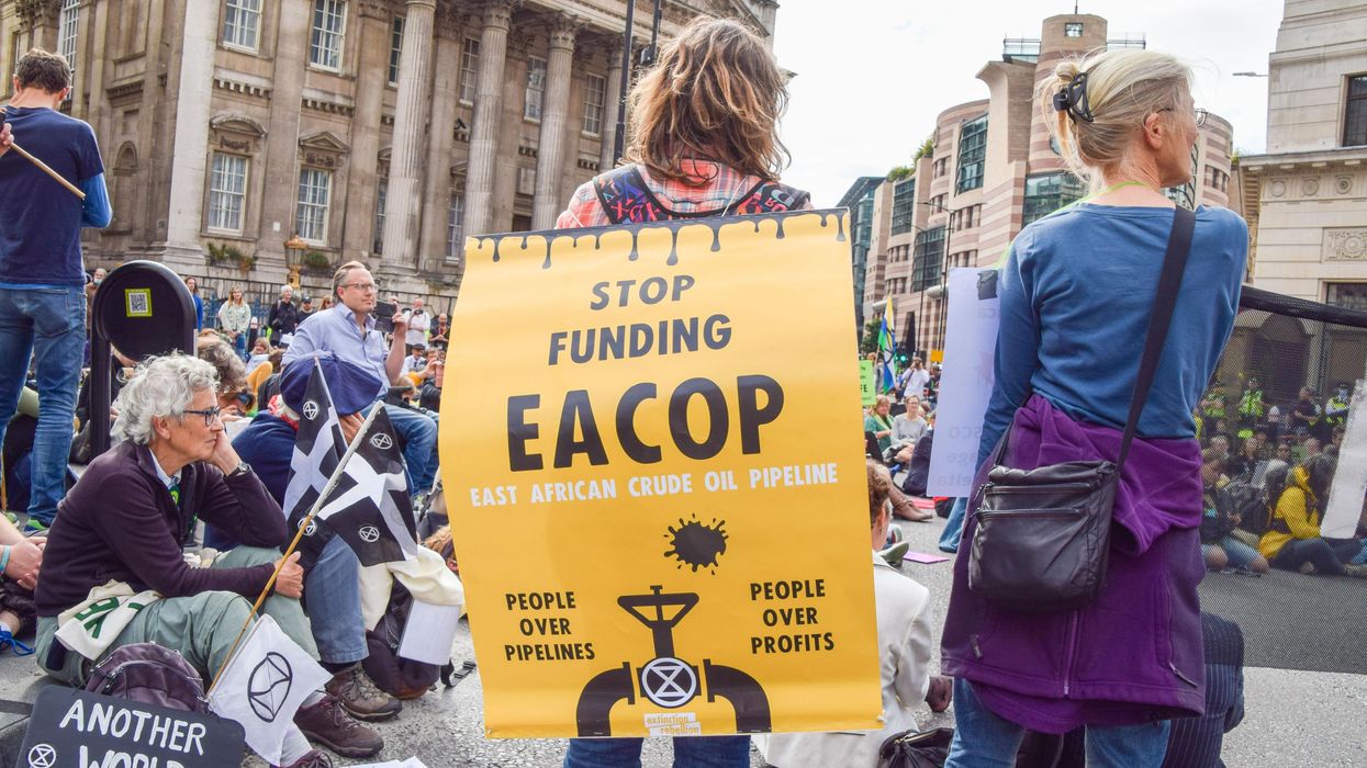 A protester carries a yellow sign protesting EACOP.
