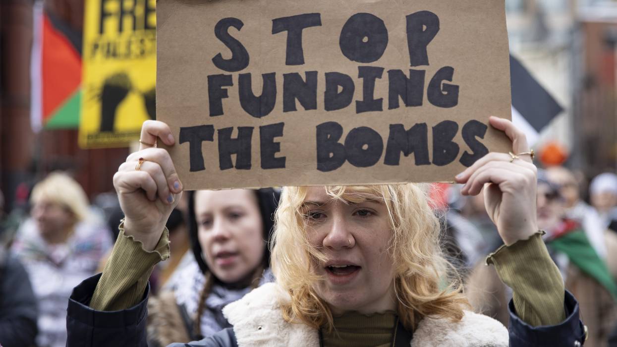 A protester holds a cardboard sign reading, "Stop funding the bombs."