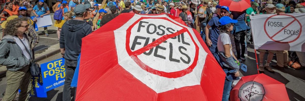 A protester holds a red umbrella reading, "Fossil fuels," crossed out with a red slash.