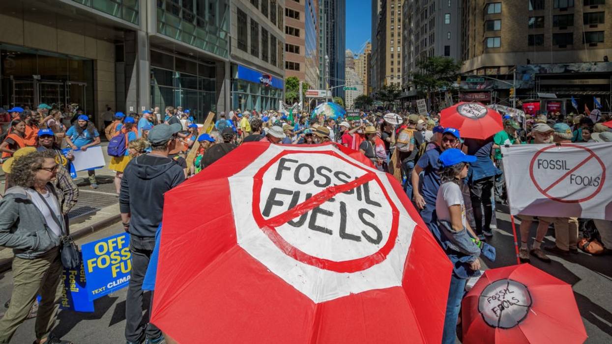 A protester holds a red umbrella reading, "Fossil fuels," crossed out with a red slash.