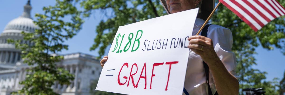 A protester holds a sign outside the US Capitol reading "$1.8B Slush Fund = Graft"