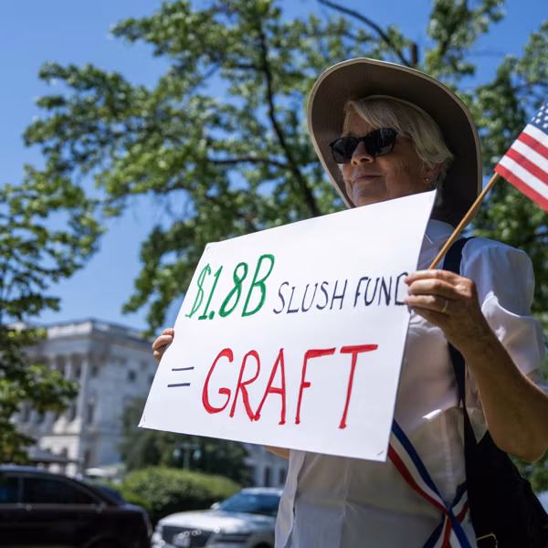 A protester holds a sign outside the US Capitol reading "$1.8B Slush Fund = Graft"