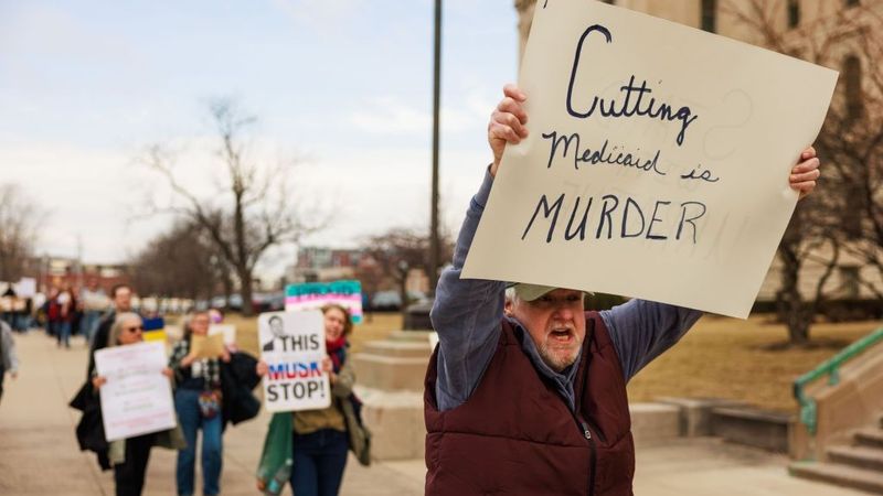 A protester holds a sign reading "Cutting Medicaid is murder."