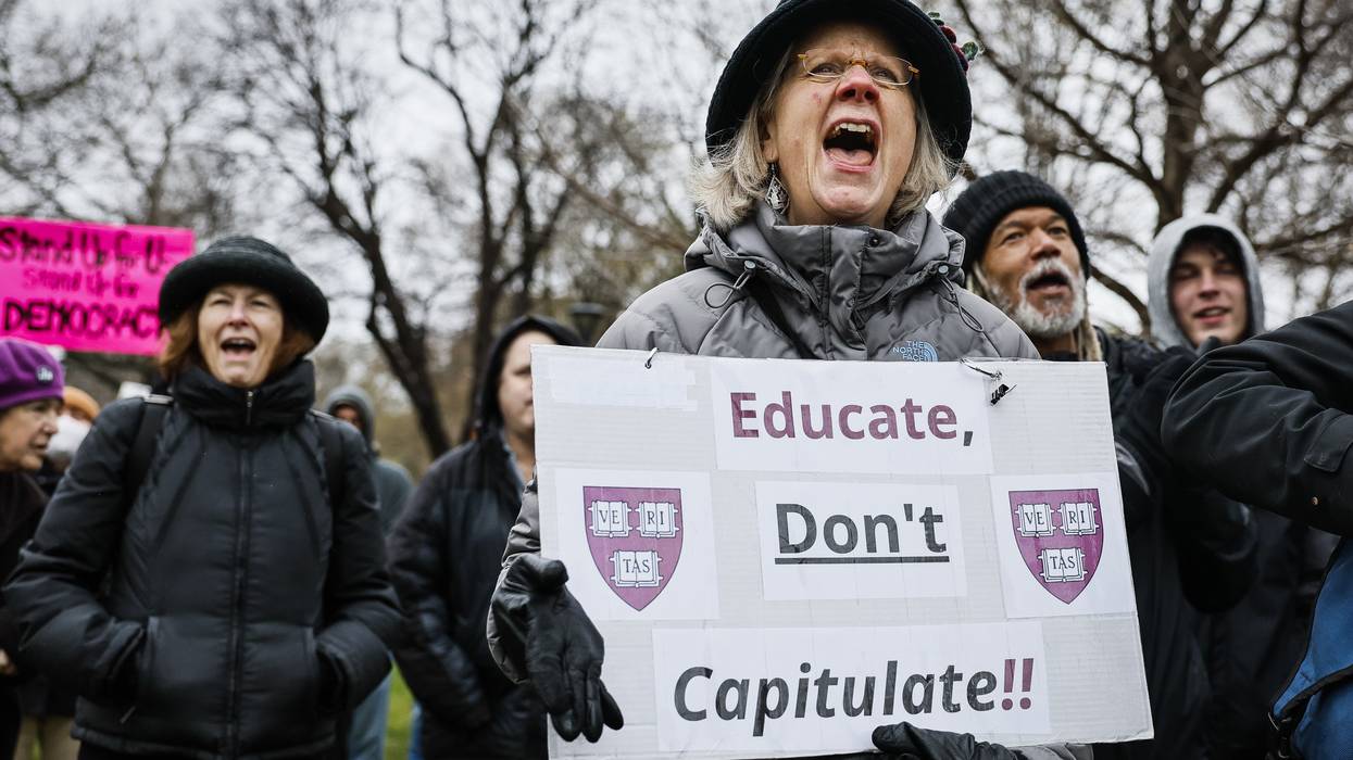 A protester holds a sign reading, "Educate, Don't Capitulate!" featuring Harvard University shields