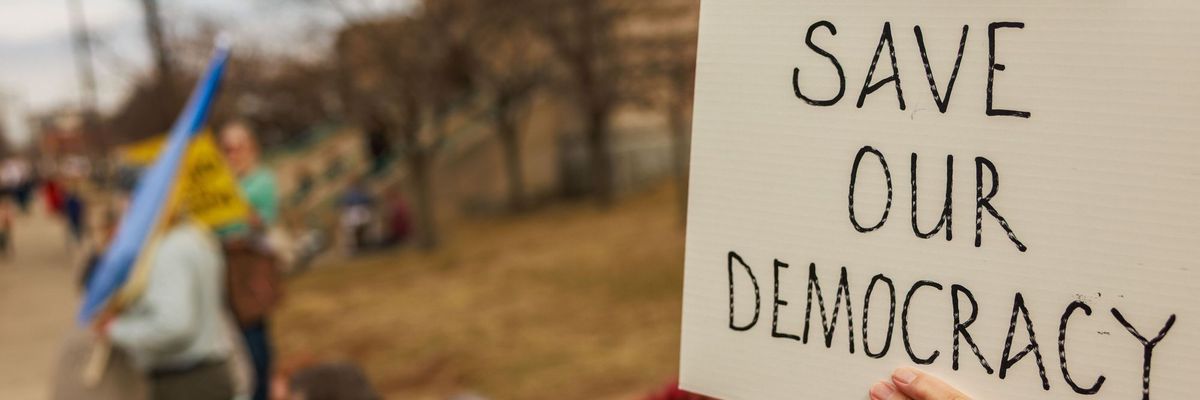 A protester holds a sign reading "Save our Democracy"...