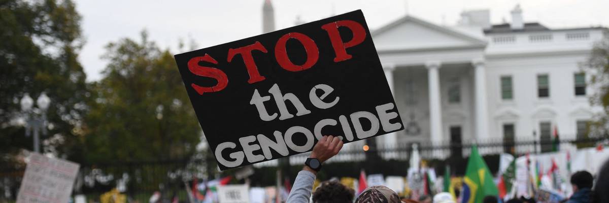 A protester holds a sign reading, "Stop the genocide" in front of the White House.