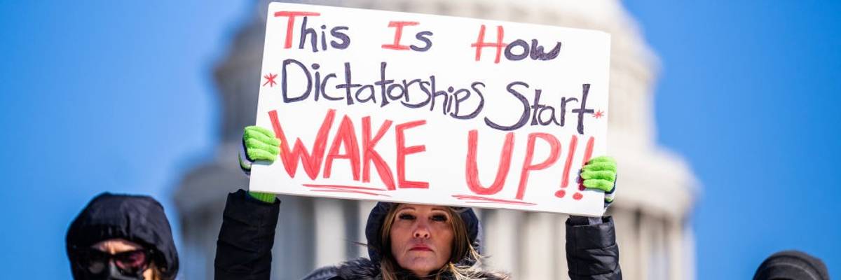 A protester holds a sign reading, "This is how dictatorships start, wake up!"
