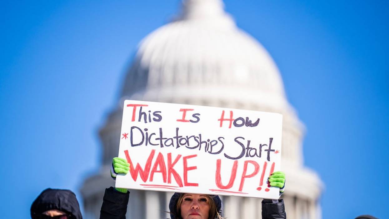 A protester holds a sign reading, "This is how dictatorships start, wake up!"