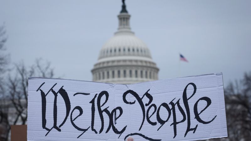 A protester holds a sign reading, "We the people" in front of the U.S. Capitol.