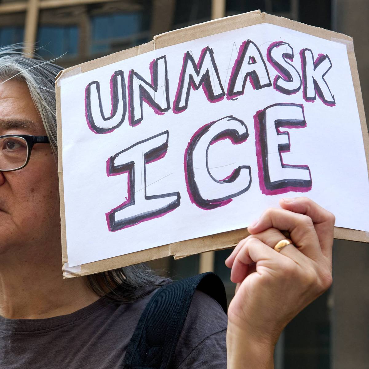 A protester holds a sign saying "Unmask ICE"