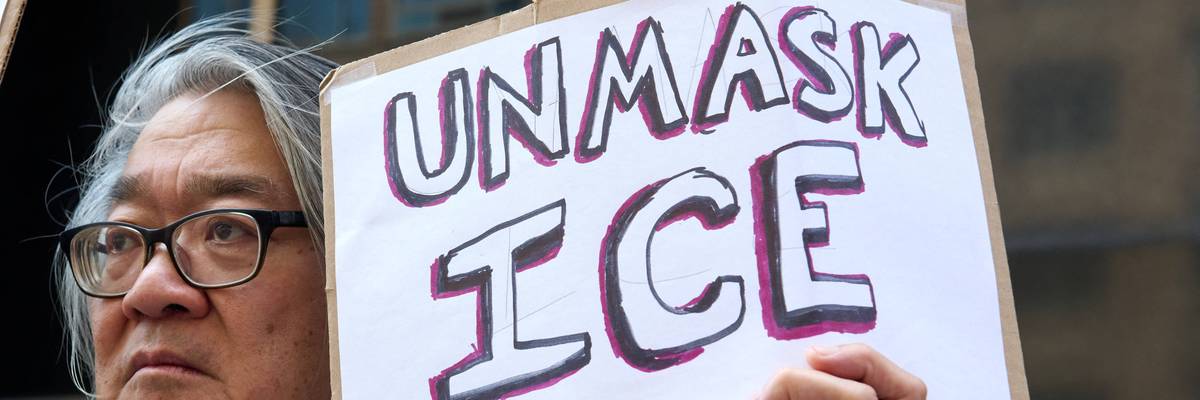 A protester holds a sign saying "Unmask ICE"