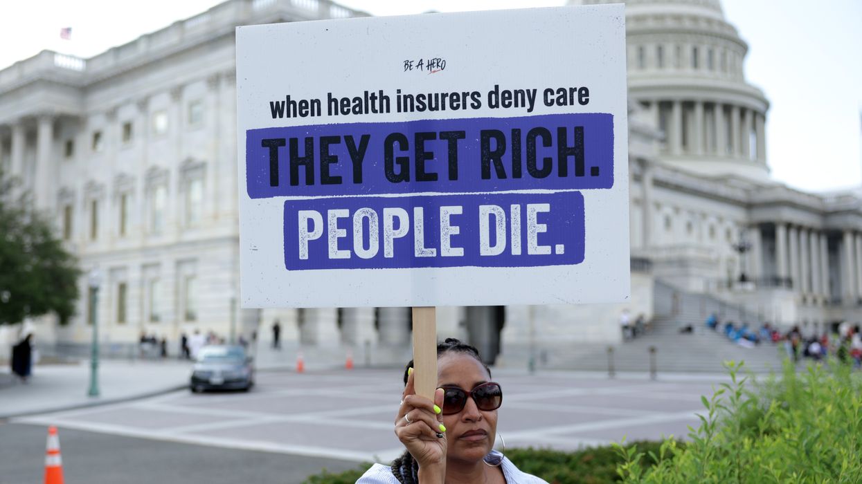 A protester holds a sign saying, "When health insurers deny care, they get rich. People die."