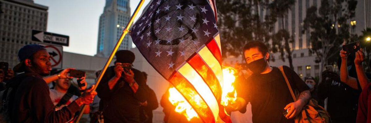 A protester holds an American flag as a fellow demonstrator lights it on fire to protest the killing of George Floyd in Minnesota by police Wednesday, May 27, 2020 in Los Angeles.