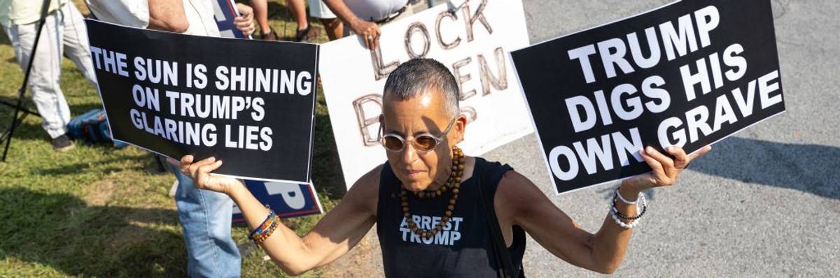 A protester holds two signs reading, "The sun is shining on Trump's glaring lies" and "Trump digs his own grave."