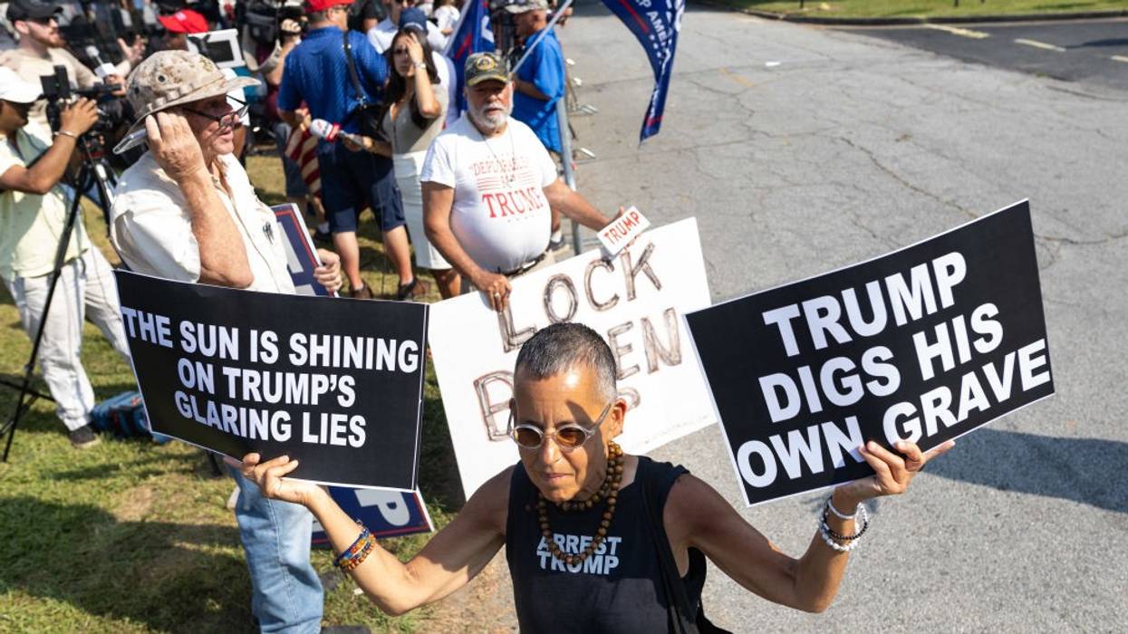 A protester holds two signs reading, "The sun is shining on Trump's glaring lies" and "Trump digs his own grave."
