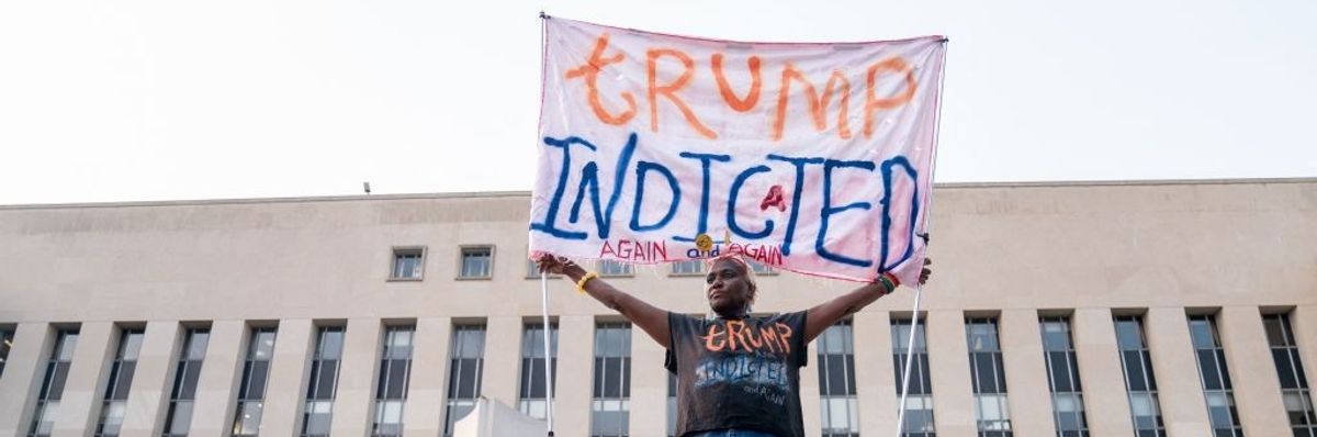 A protester holds up a sign saying, "Trump indicted again and again."