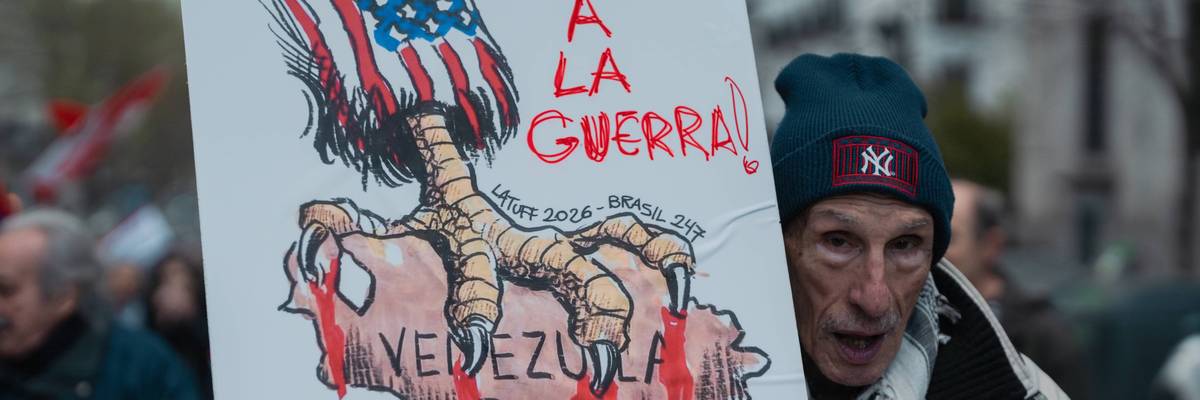 A protester in Madrid holds a sign showing the US with talons on Venezuela and the words "stop the war!"