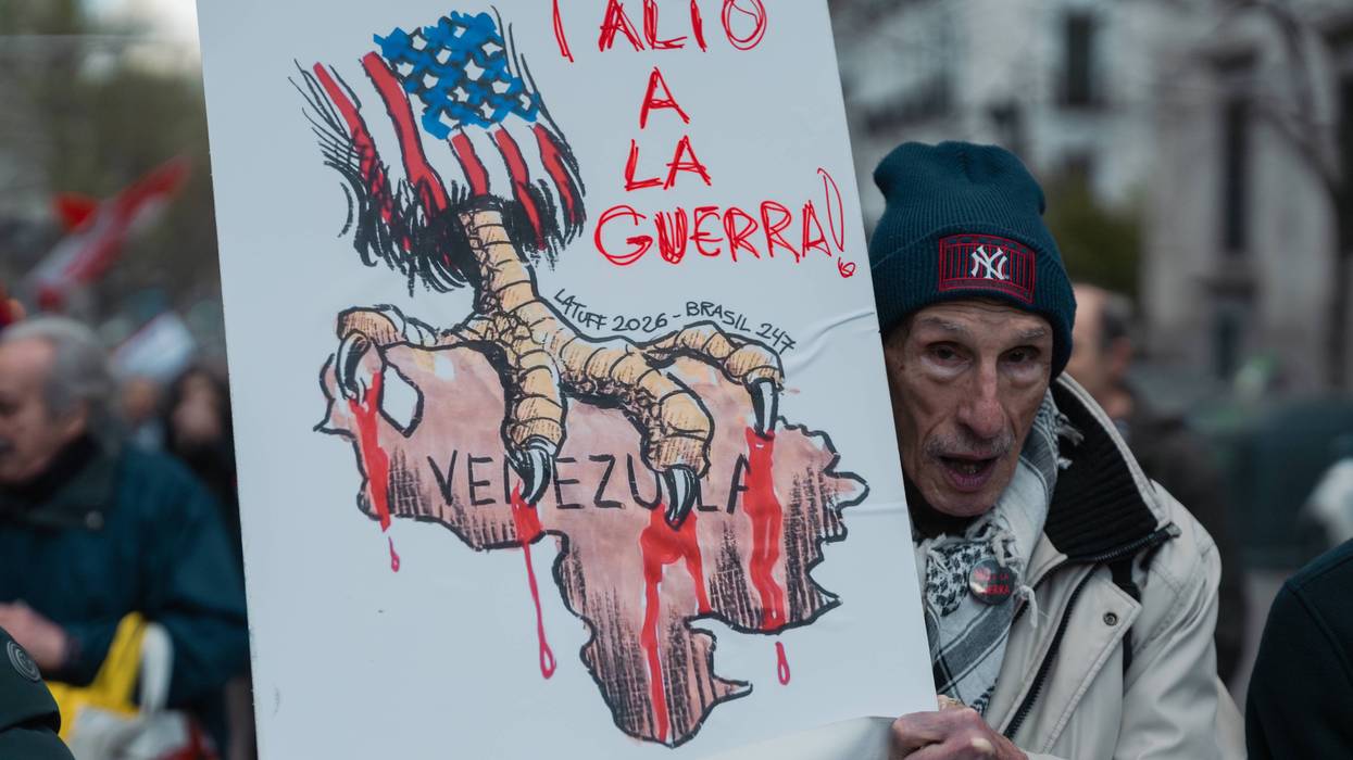 A protester in Madrid holds a sign showing the US with talons on Venezuela and the words "stop the war!"