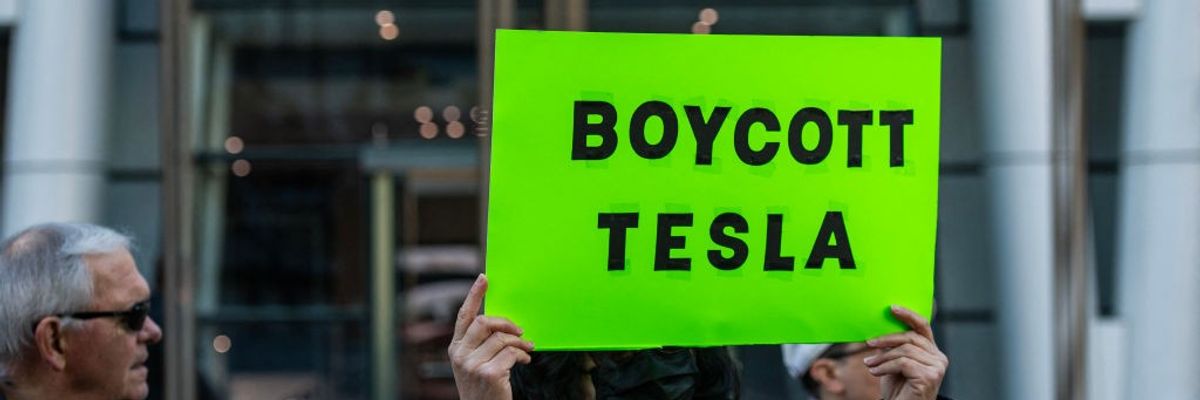 A protester stands outside a Tesla dealership with a sign reading, "Boycott Tesla."