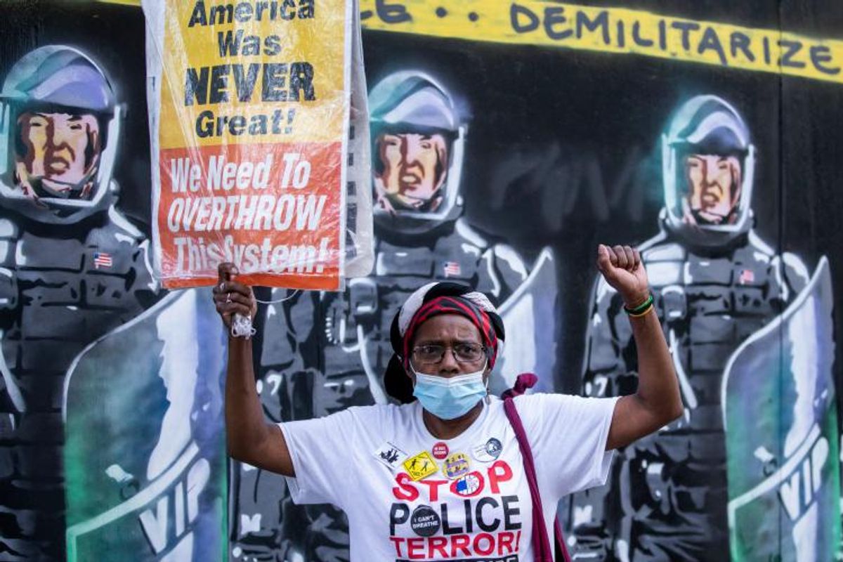 https://www.commondreams.org/media-library/a-protester-wearing-a-mask-holds-a-sign-that-reads-american-was-never-great-we-need-to-overthrow-this-system-in-front-of-a.jpg?id=32144082&width=1200&height=800&quality=90&coordinates=0%2C0%2C205%2C0