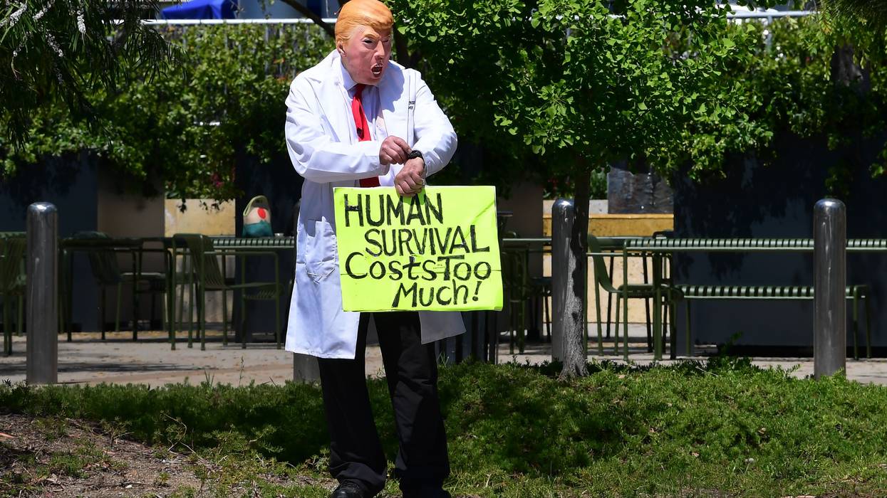 A protester wearing a Trump holds a sign that reads "Human survival costs too much"