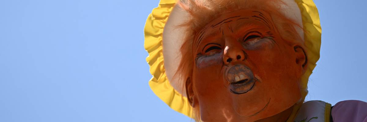 A protester wears a mask of Donald Trump in a bonnet.