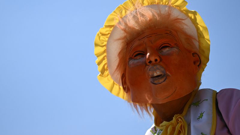 A protester wears a mask of Donald Trump in a bonnet.