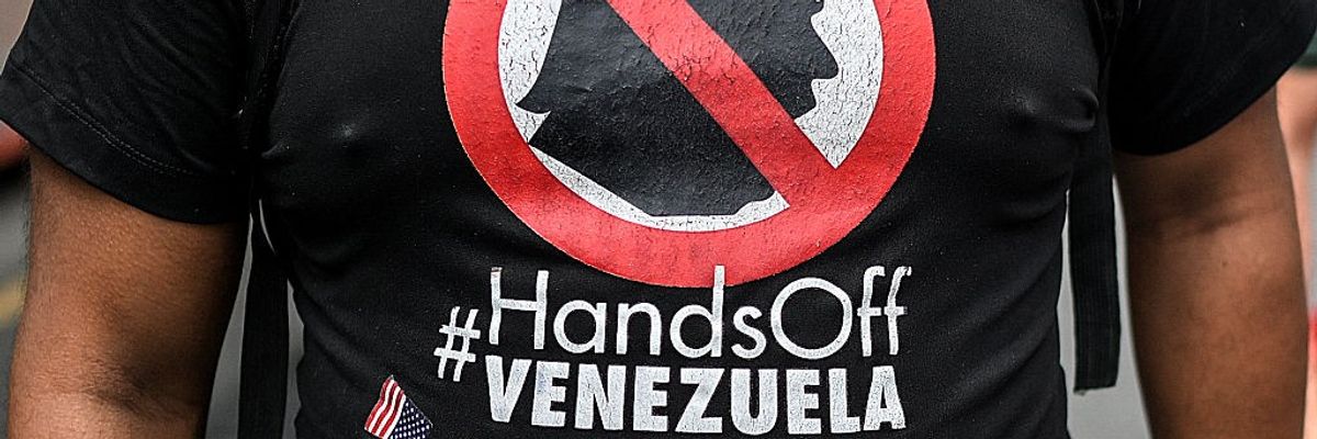 A protester wears a shirt saying, "Hands off Venezuela" below a crossed-out Trump silhouette.
