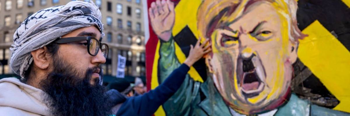 A protestor stands infront of an image of Trump dressed as Hitler.