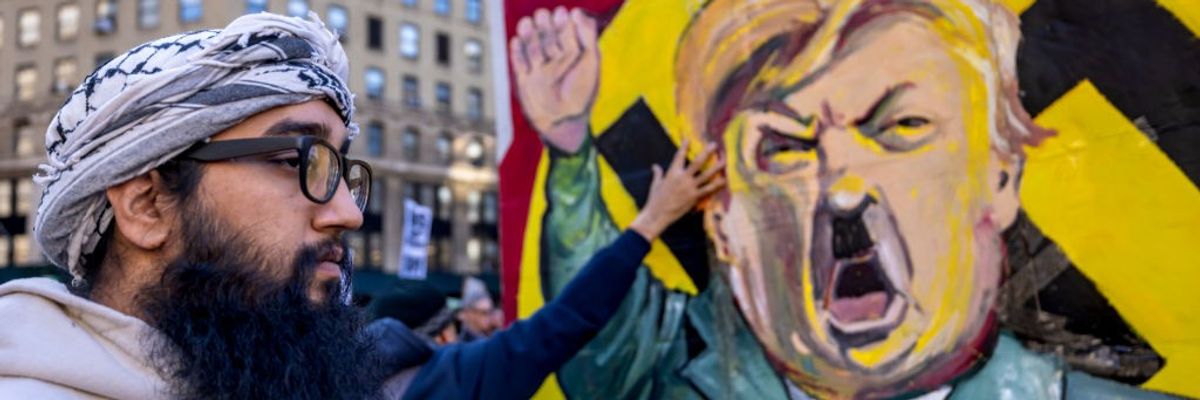 A protestor stands infront of an image of Trump dressed as Hitler