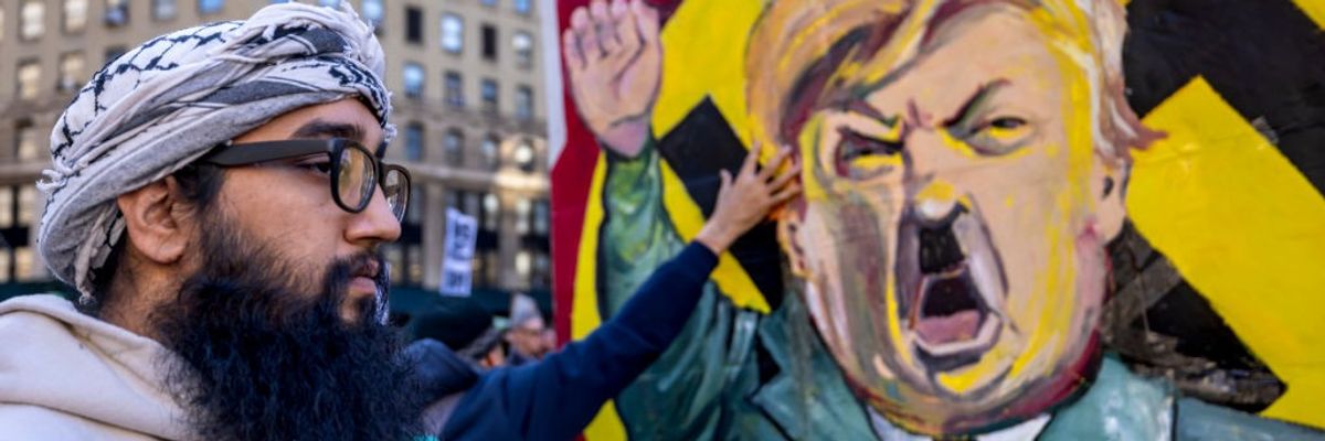 A protestor stands infront of an image of Trump dressed as Hitler.