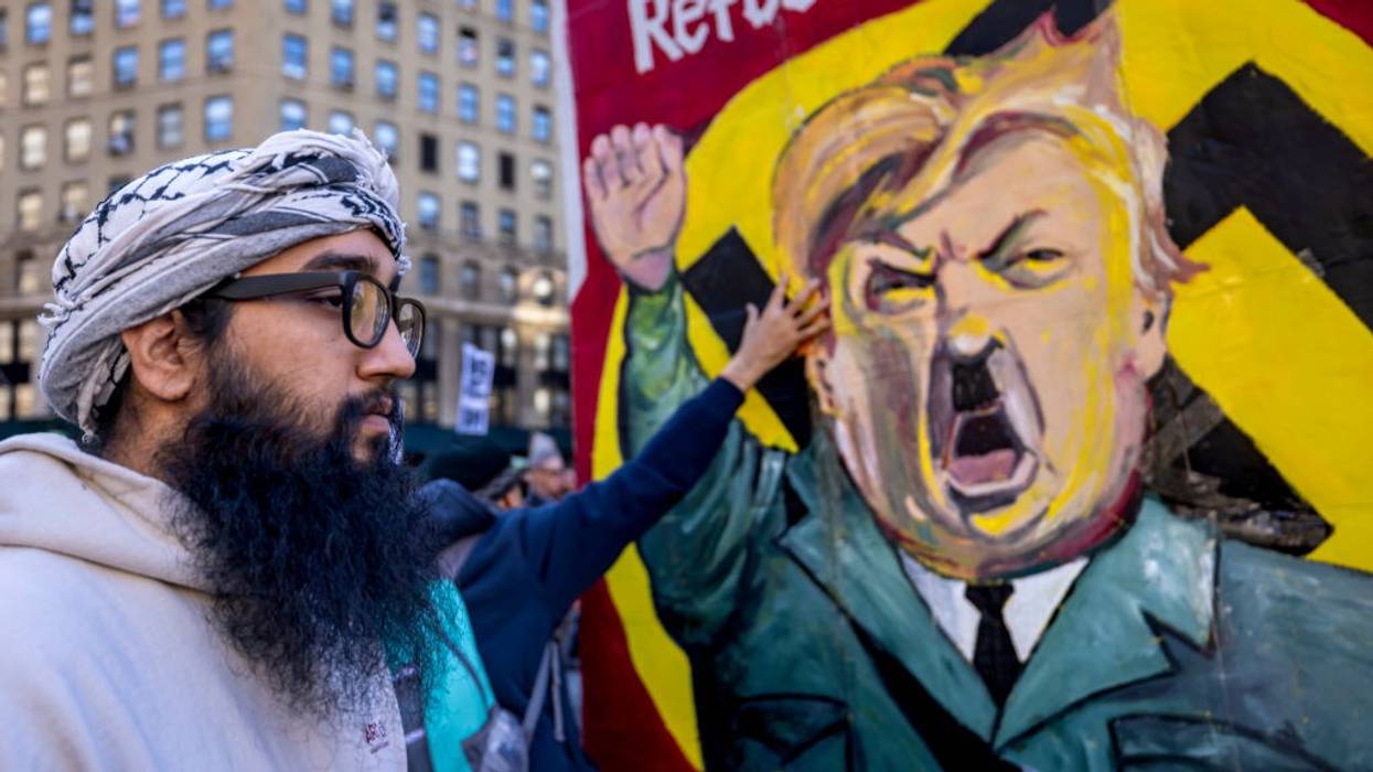 A protestor stands infront of an image of Trump dressed as Hitler