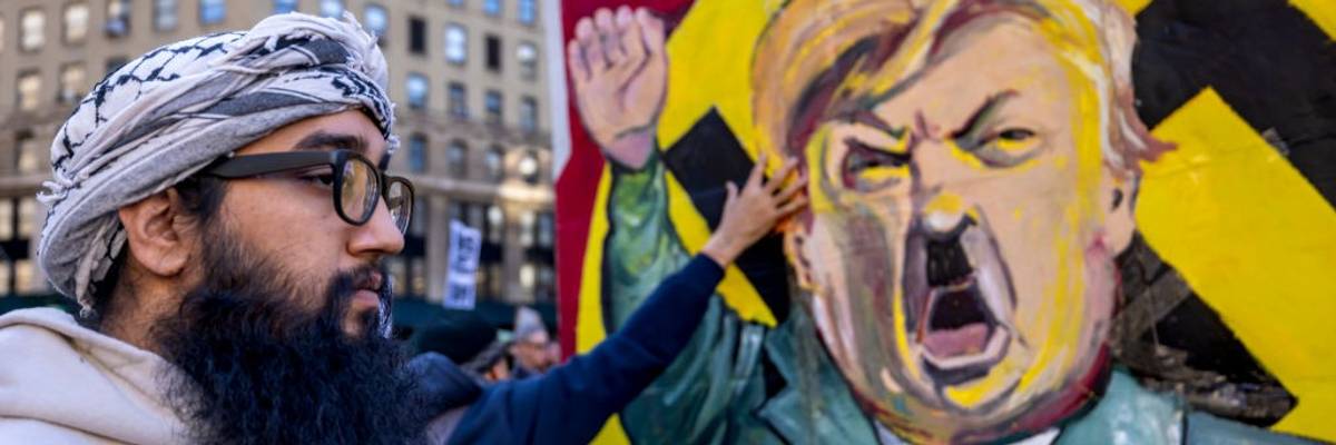 A protestor stands infront of an image of Trump dressed as...