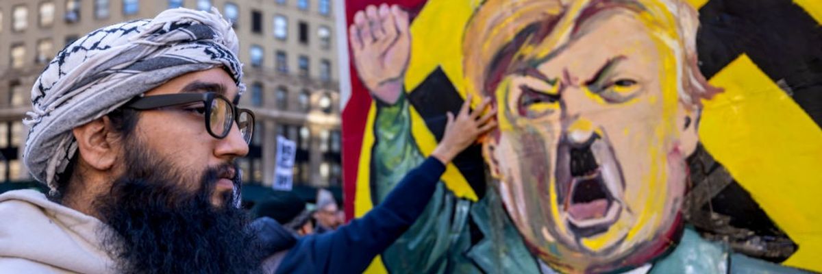 A protestor stands infront of an image of Trump dressed as...