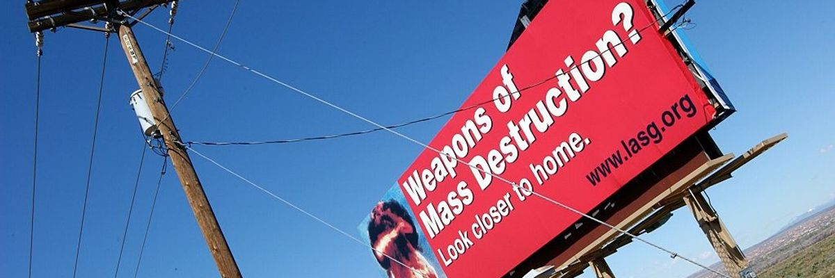 A red billboard against a blue sky reading, "Weapons of mass destruction? Look closer to home."