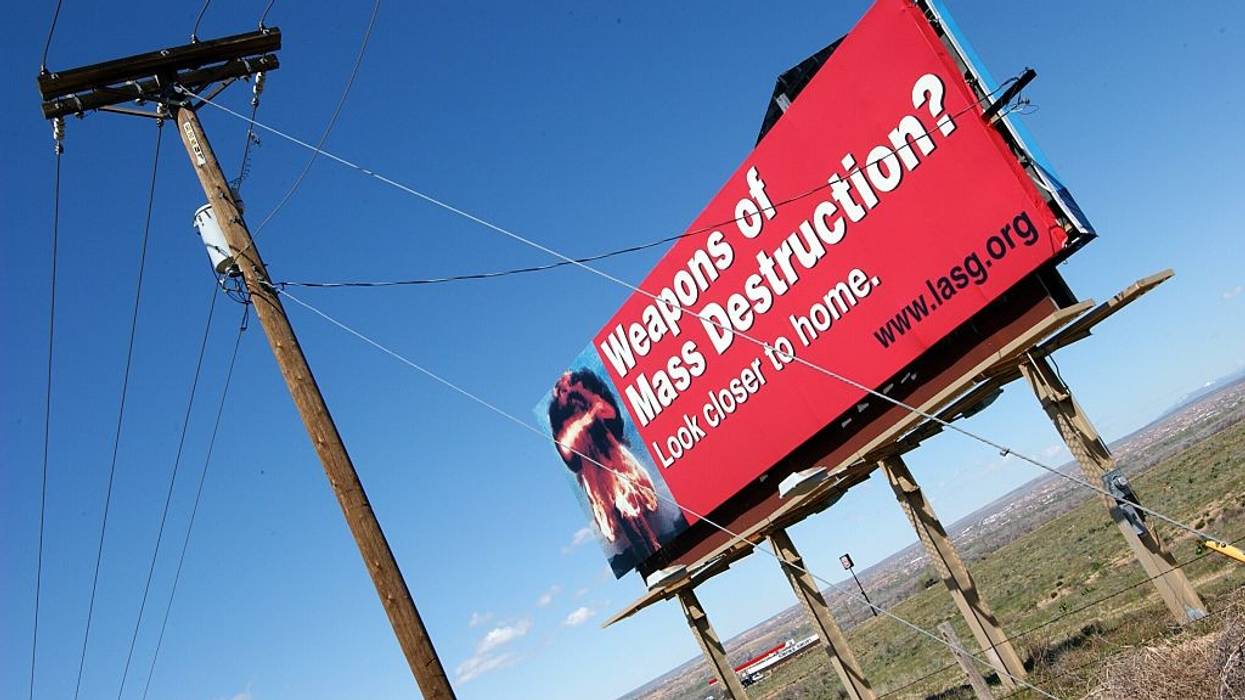 A red billboard against a blue sky reading, "Weapons of mass destruction? Look closer to home."