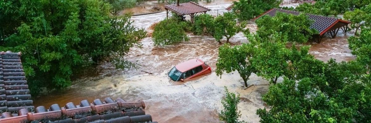 A red car submerged in rushing flood waters.