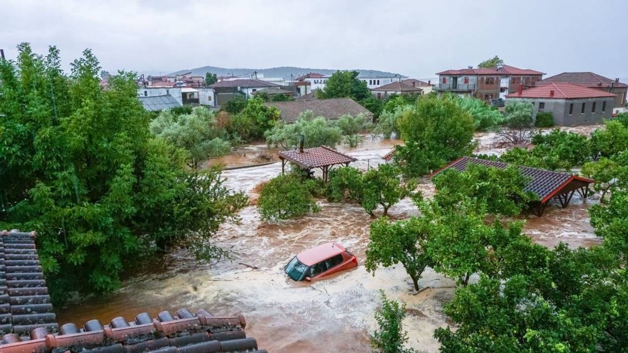A red car submerged in rushing flood waters.