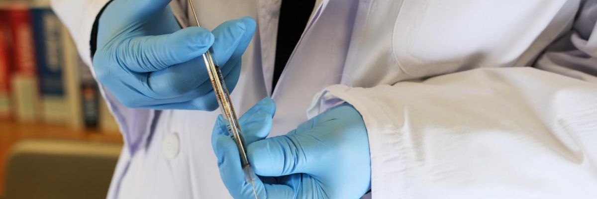 A researcher holds a syringe over test vials.