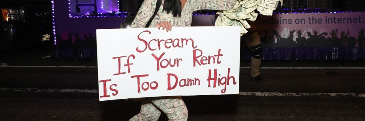 A reveler roller skates with a sign reading, “Scream If Your Rent Is Too Damn High.” 