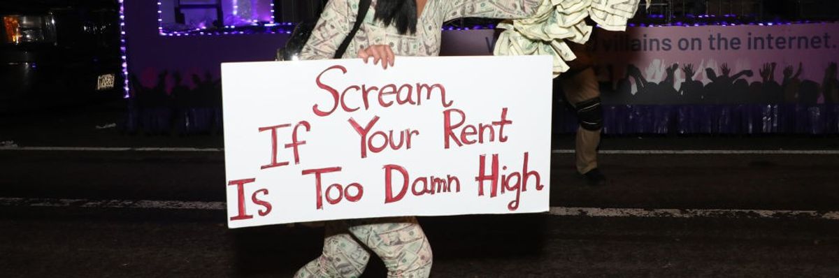 A reveler roller skates with a sign reading, “Scream If Your Rent Is Too Damn High.” 