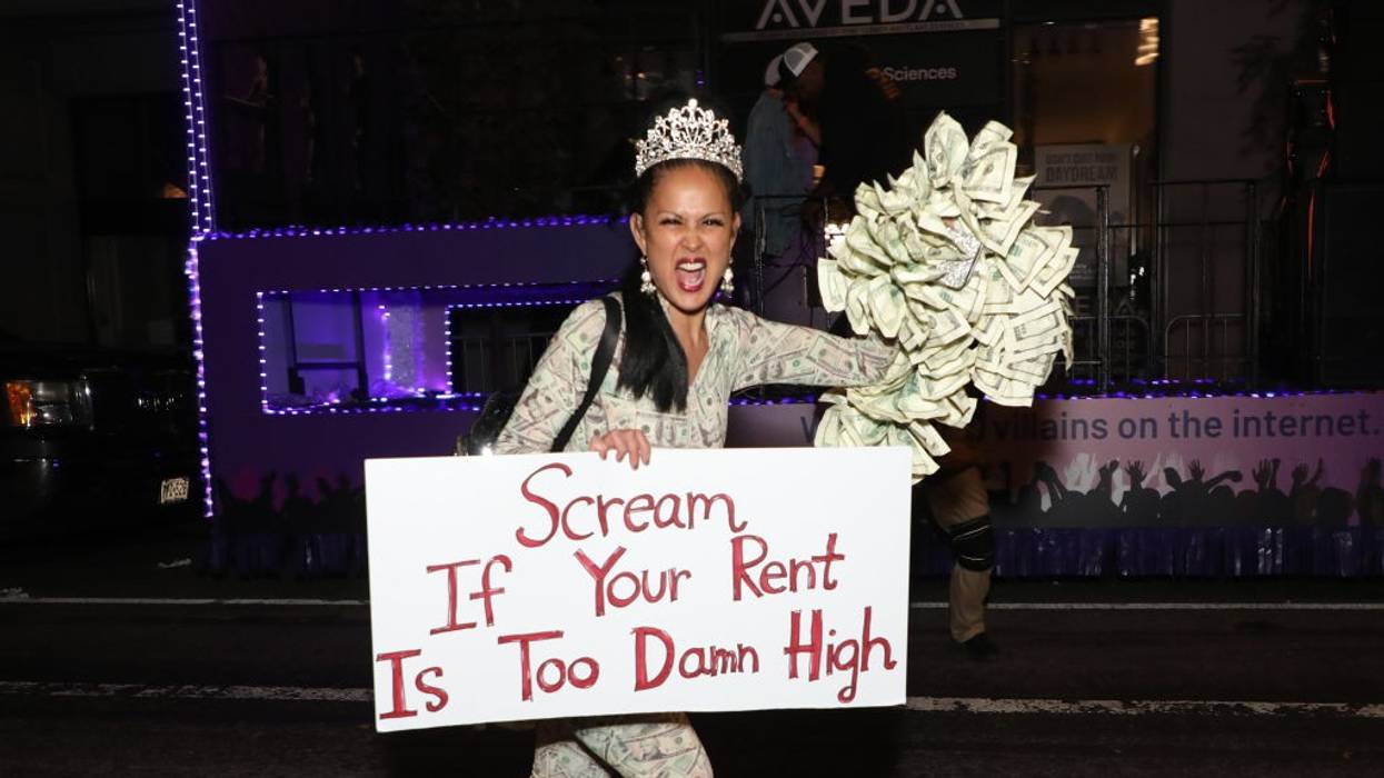 A reveler roller skates with a sign reading, “Scream If Your Rent Is Too Damn High.”