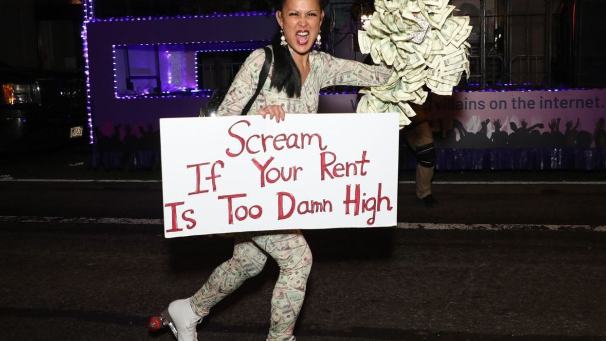 A reveler roller skates with a sign reading, “Scream If Your Rent Is Too Damn High.”
