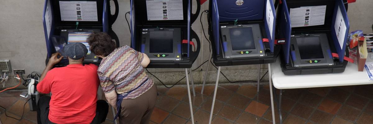 A senior woman assisting a man in an electric scooter at the voting machines for early voting at the Stephen P. Clark Government Center.
