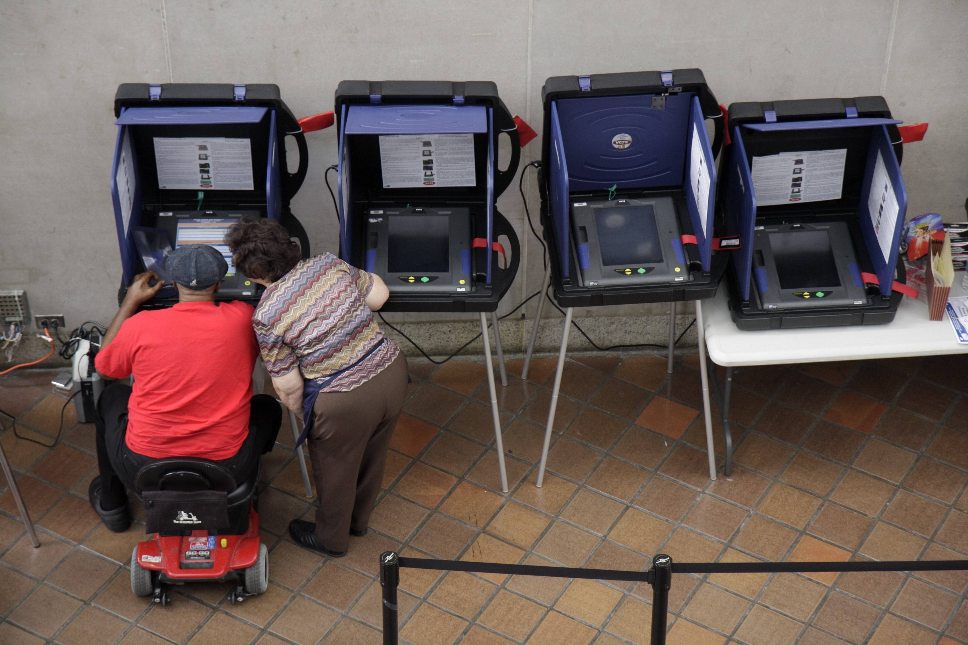 A senior woman assisting a man in an electric scooter at the voting machines for early voting at the Stephen P. Clark Government Center.